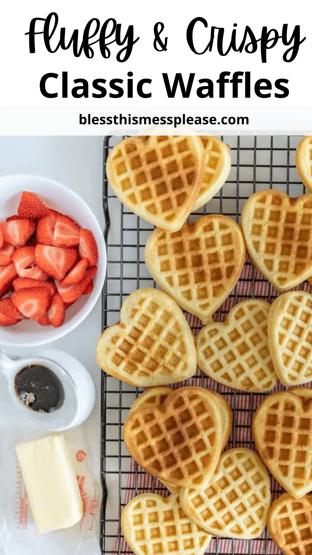 Heart-shaped waffles cool on a wire rack, accompanied by a bowl of sliced strawberries, a glass syrup dispenser, and a stick of butter. The text reads Fluffy & Crispy Classic Waffles Recipe with a website link below.