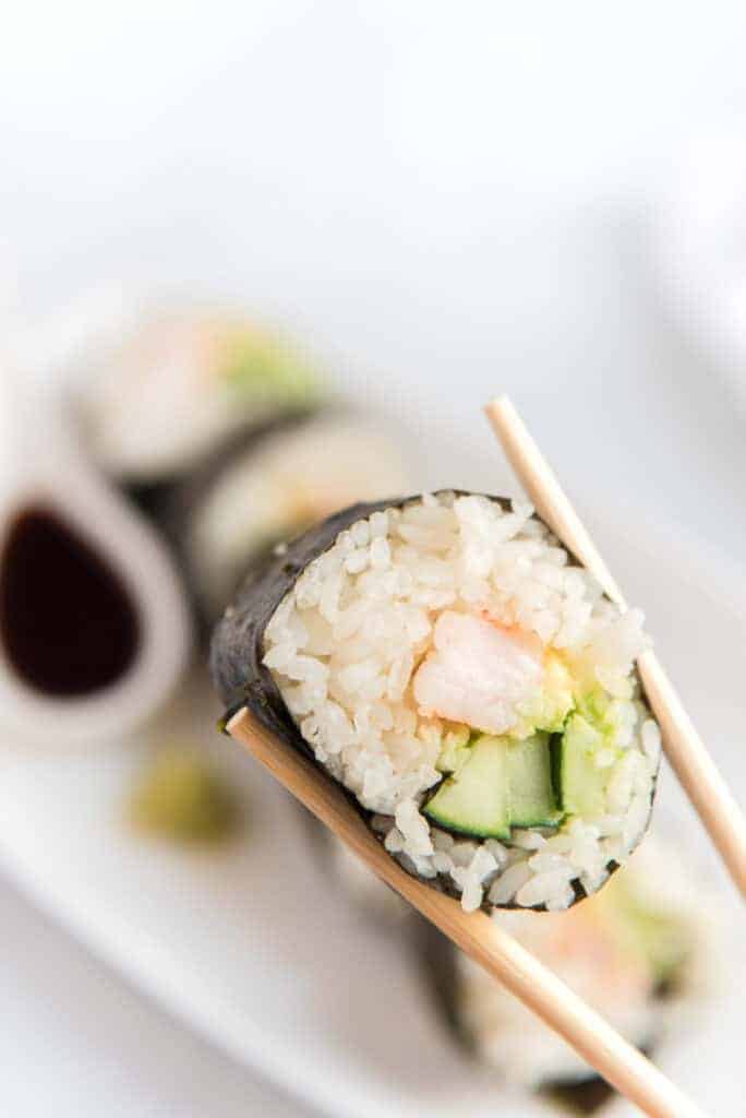 close up of chopsticks holding a shrimp sushi roll