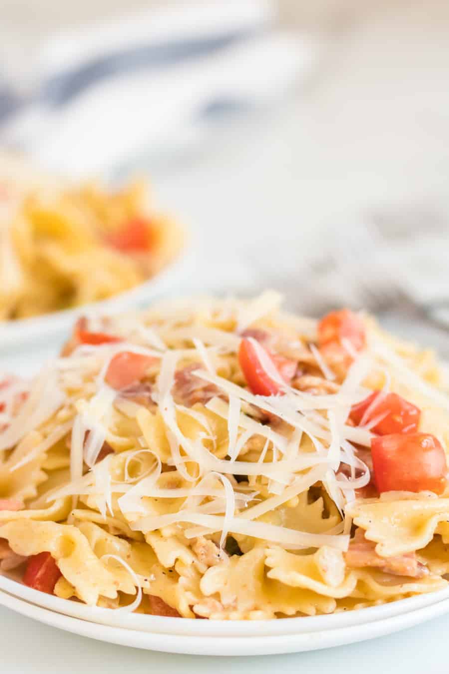 Pasta with bacon, tomatoes, green peppers, and shaved Parmesan cheese on a white plate with a fork. 