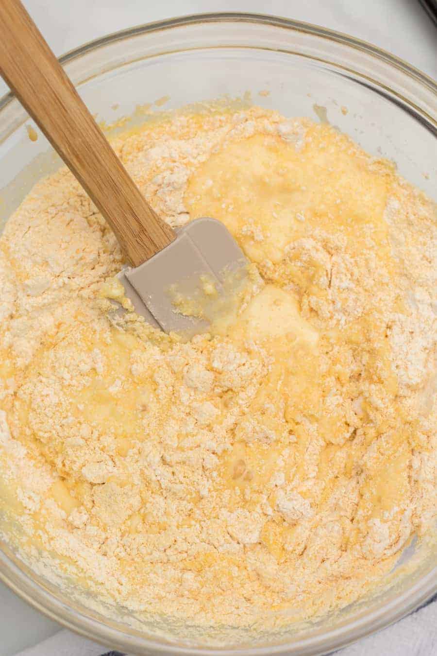 Pâte à muffins de maïs dans un bol à mélanger en verre avec une spatule en caoutchouc gris posée sur le côté.