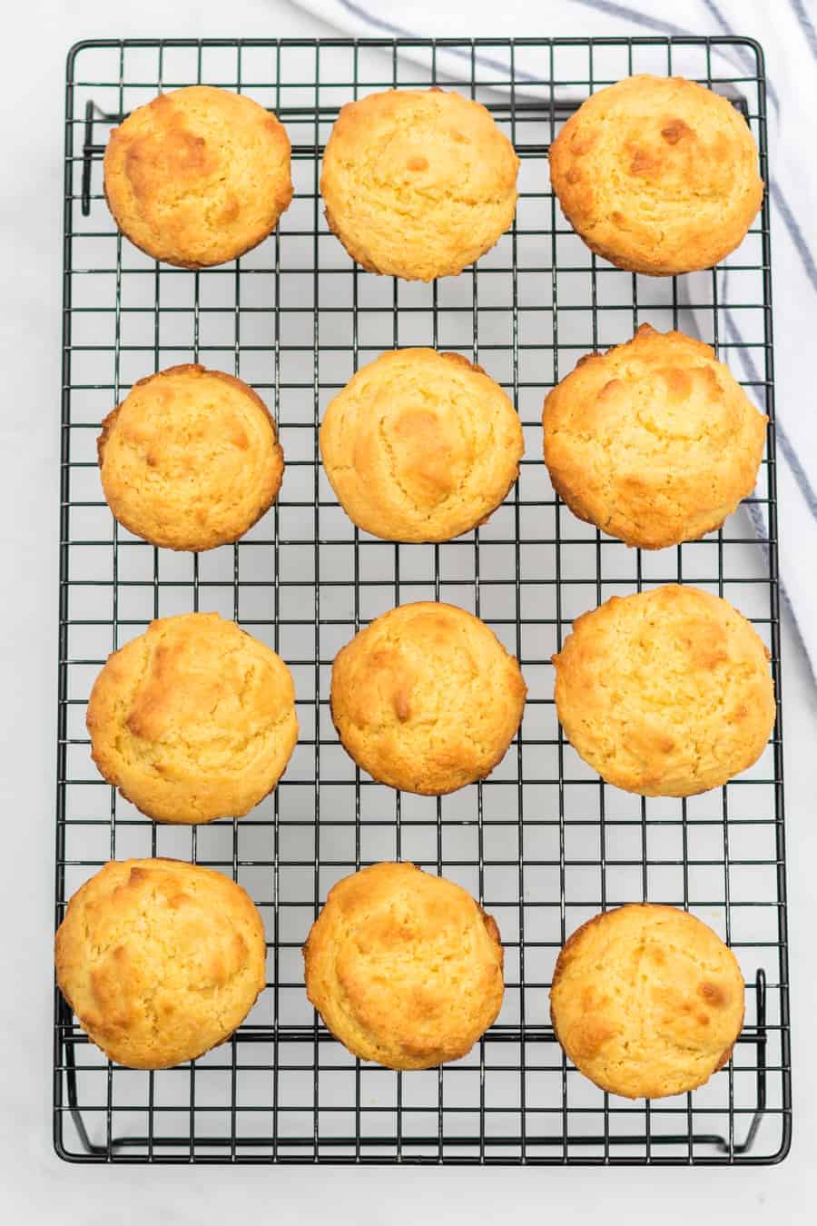 12 muffin di mais al forno e dorati poggiano su un rack di raffreddamento a filo.