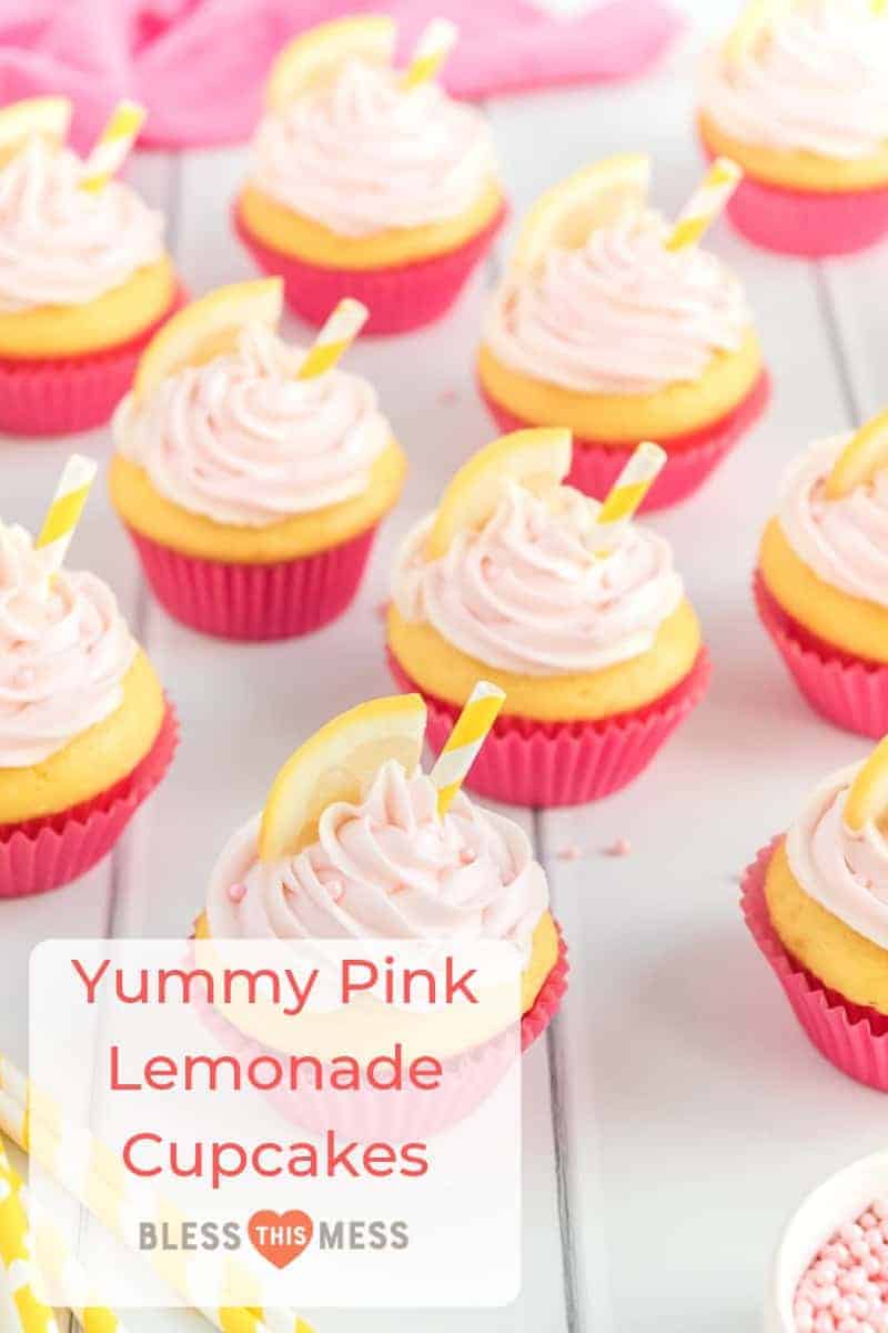 yellow cupcakes in bright pink wrappers with light pink frosting, pink sprinkles, a lemon slice, and a yellow and white straw on a white table.