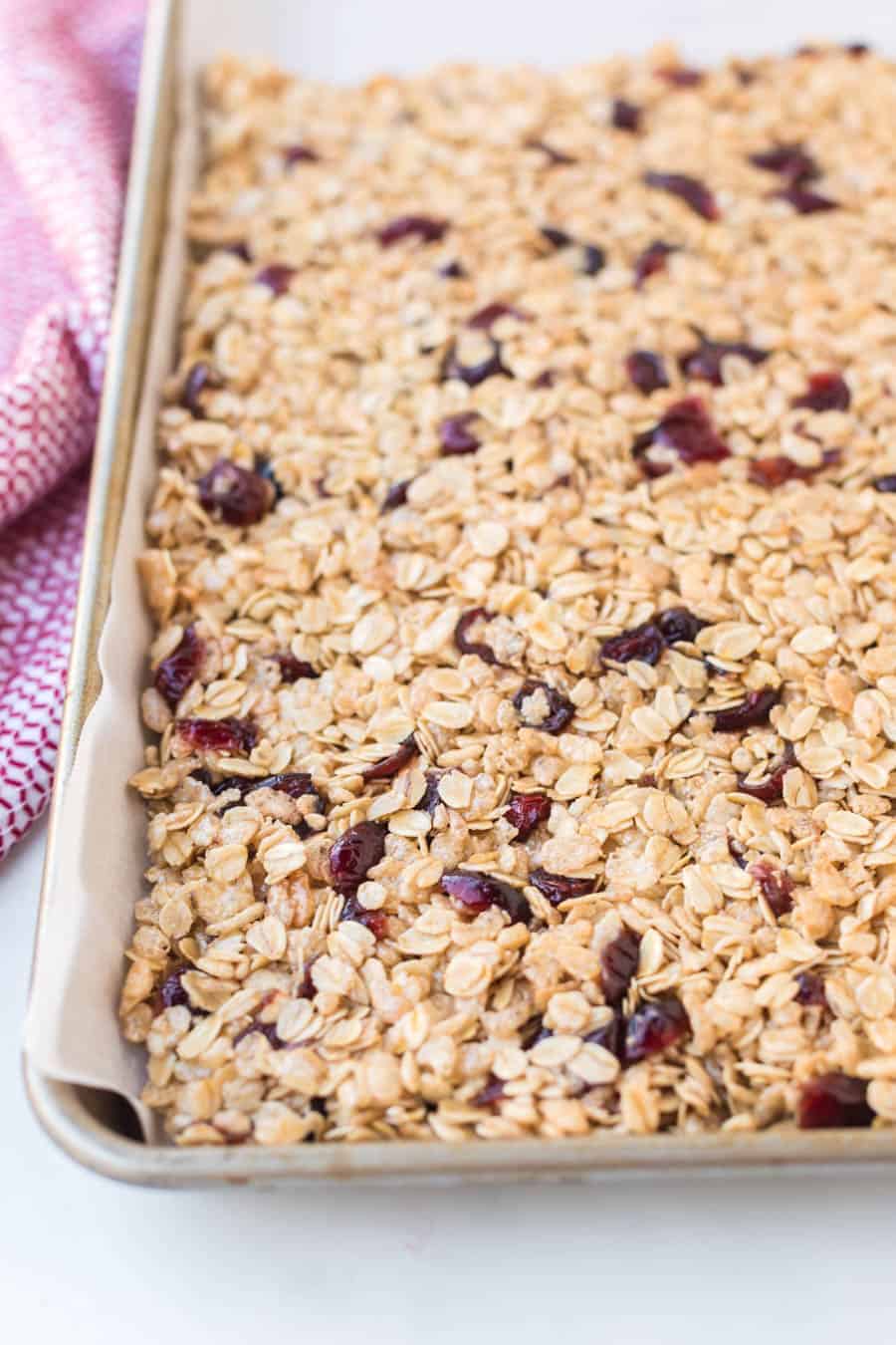 a baking sheet with parchment and whole cranberry granola bars pressed out.