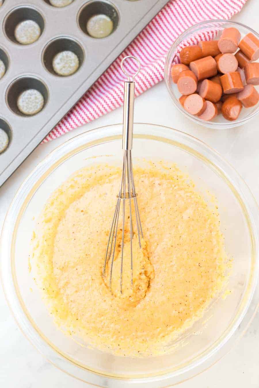 cornbread dough in a clear bowl with a whisk.