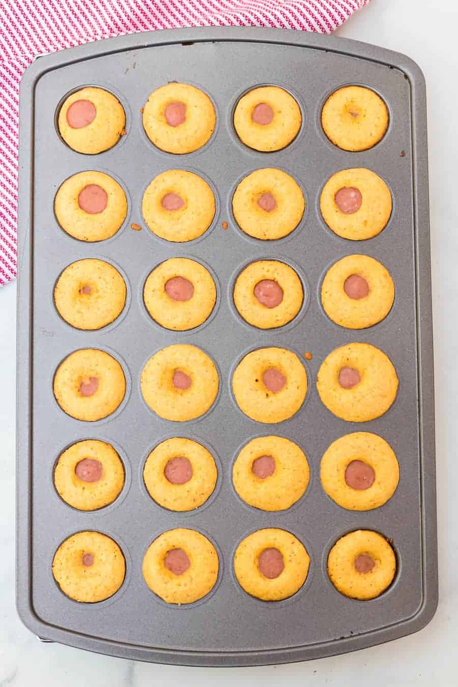 a muffin tin with cornbread mix and hot dogs inside - baked.