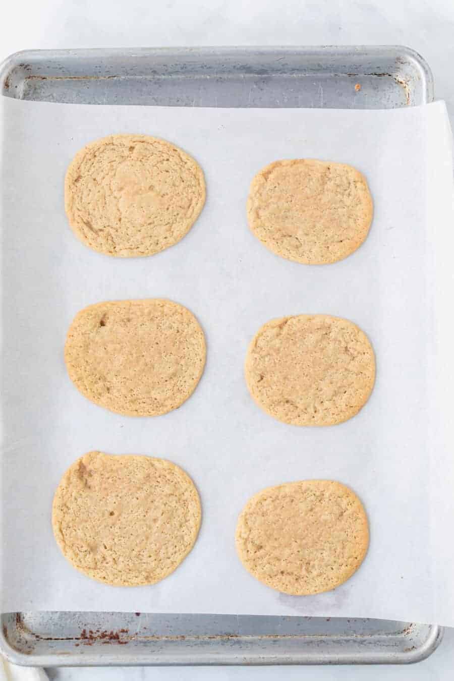 a sheet pan and white parchment with six thin golden cookies.