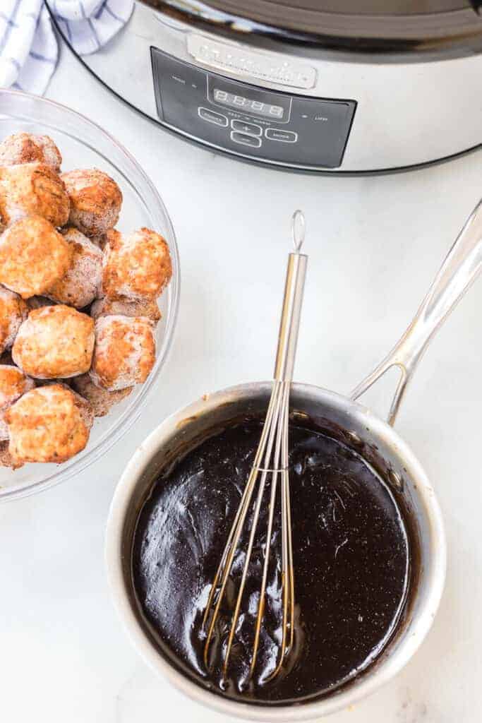 meatballs in a clear bowl next to a pot of honey teriyaki sauce
