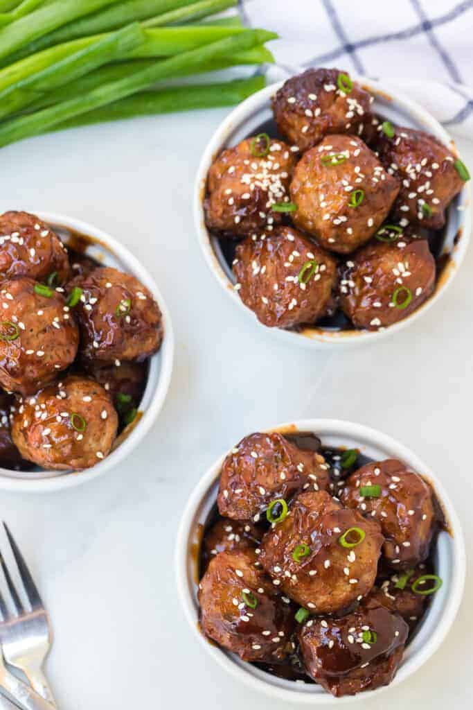 top view of white serving dish of honey teriyaki meatballs with sesame seeds and green onion on top