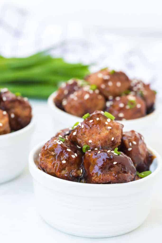 white serving dish of honey teriyaki meatballs with sesame seeds and green onion on top