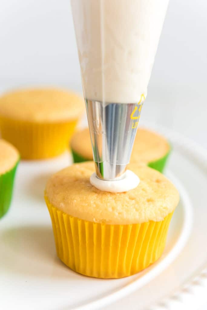 buttercream icing being piped onto vanilla cupcakes