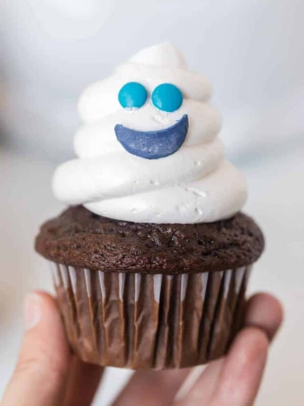 a chocolate cupcake with white frosting piped to a ghost shape with a smiley face