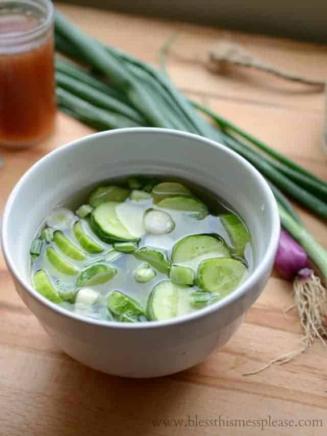 cucumbers soaking in a brine in white bowl onion stalks in background.