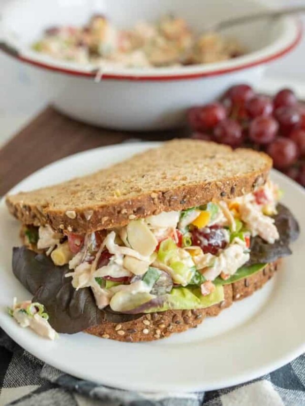 close up picture of a chicken salad sandwich with a bowl of chicken salad and gob of grapes in the background