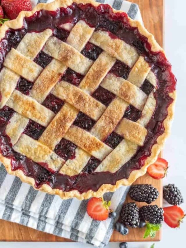 picture of triple berry pie on a wood board with fresh berries in front