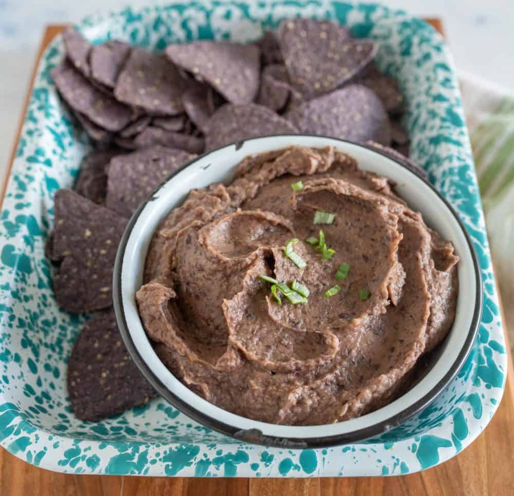 close up of a bowl of black bean dip on a tray with tortilla chips