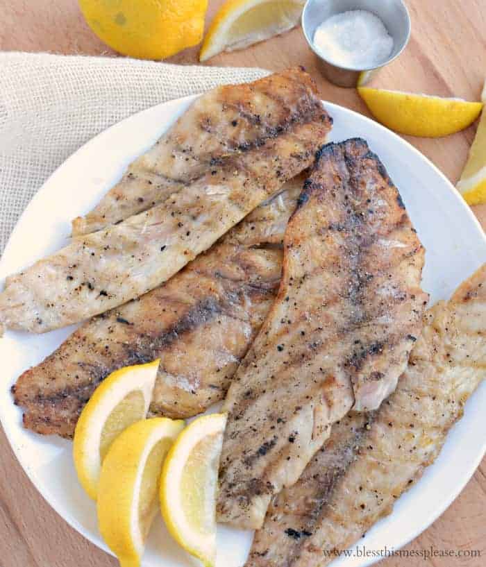 Grilled fish topped with parsley and lemon slices.