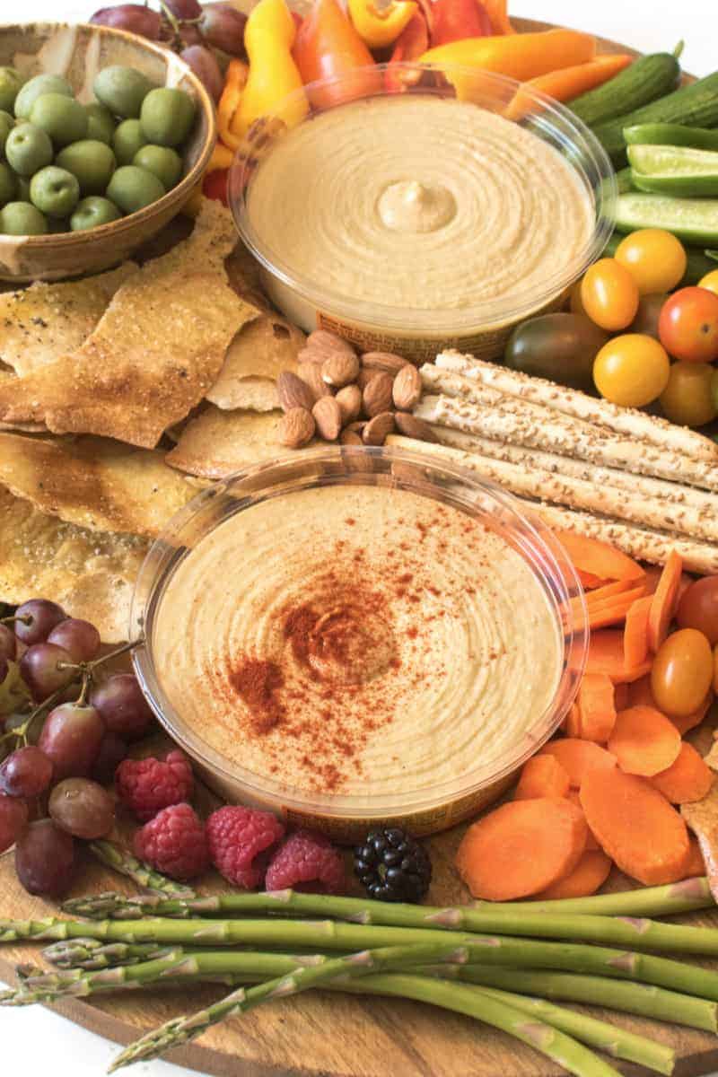 Close-up of a Simple DIY Hummus Platter with assorted cracker and nuts and olives and veggies on a wooden board. 