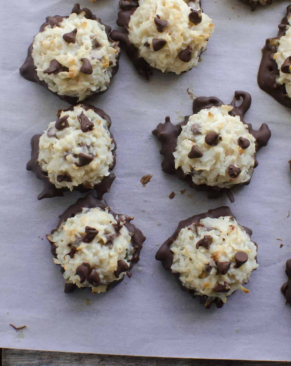 Top view of a coconut macaroons with mini chocolate chips on top and the bottoms dipped in chocolate sitting on a piece of white parchment paper. 