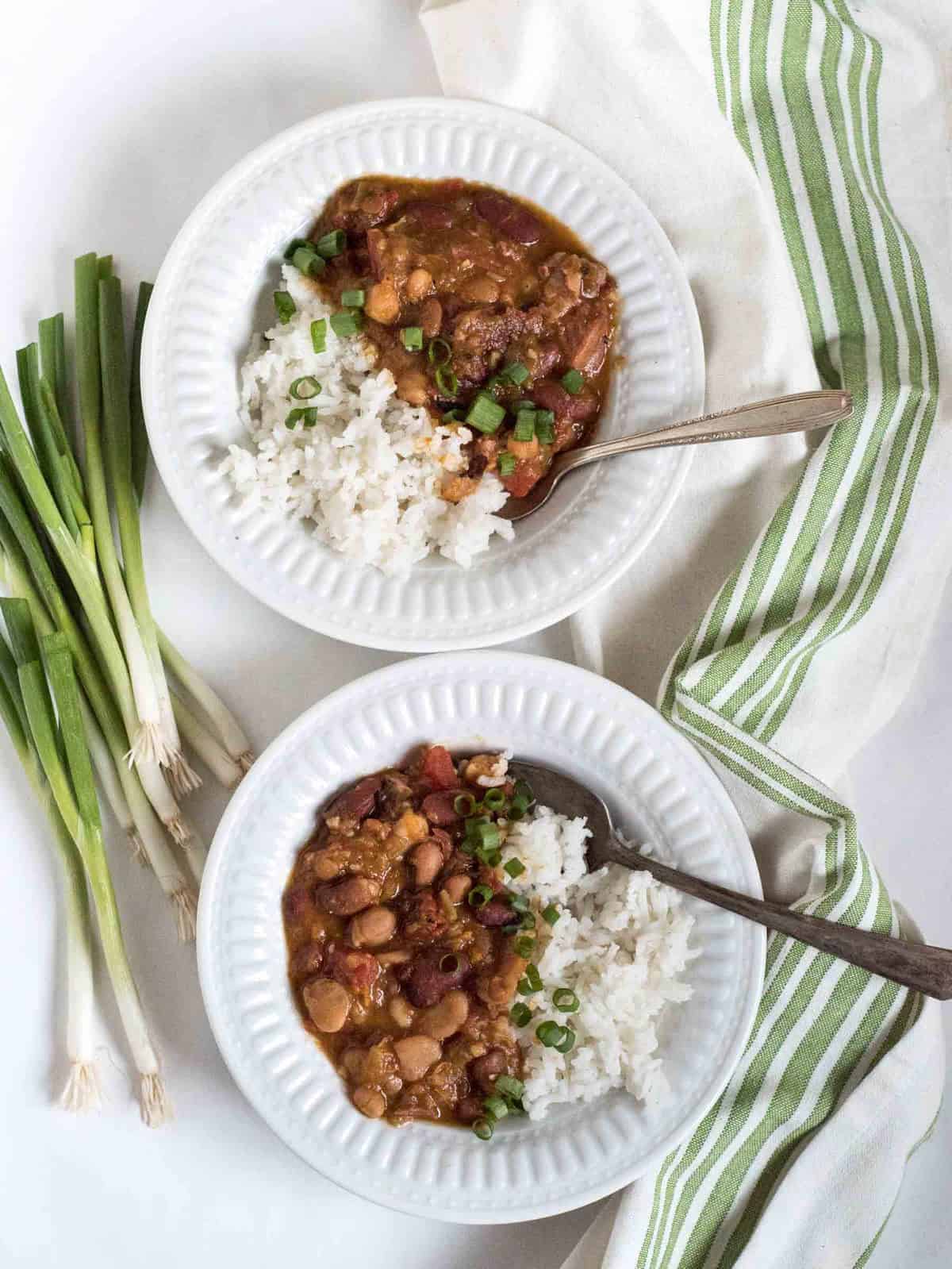 two bowls of beans and rice topped with chopped green onions on a white and green towel