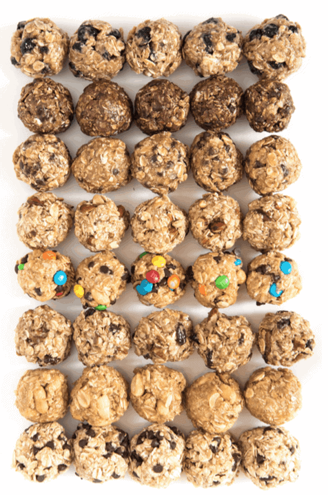 Rows of bite-sized no bake energy bites with various mix-ins, including chocolate chips, oats, and colorful candy pieces, arranged neatly on a white surface.