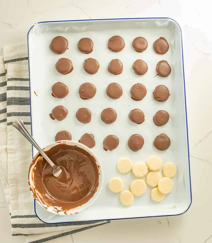 a tray with dipped peppermint patties, undipped peppermint patties, and a bowl of melted chocolate with a fork resting in it