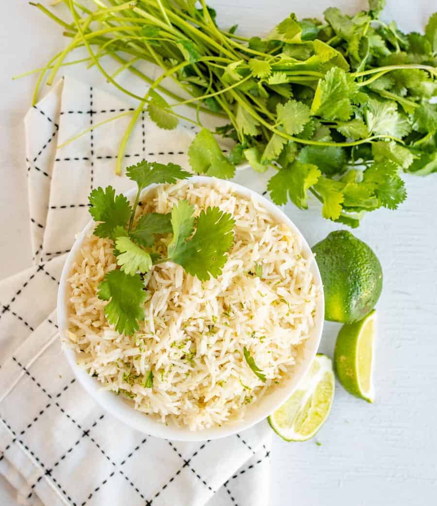 a bowl of cilantro lime rice topped with fresh cilantro. Bowl is surrounded by cilantro and limes. 