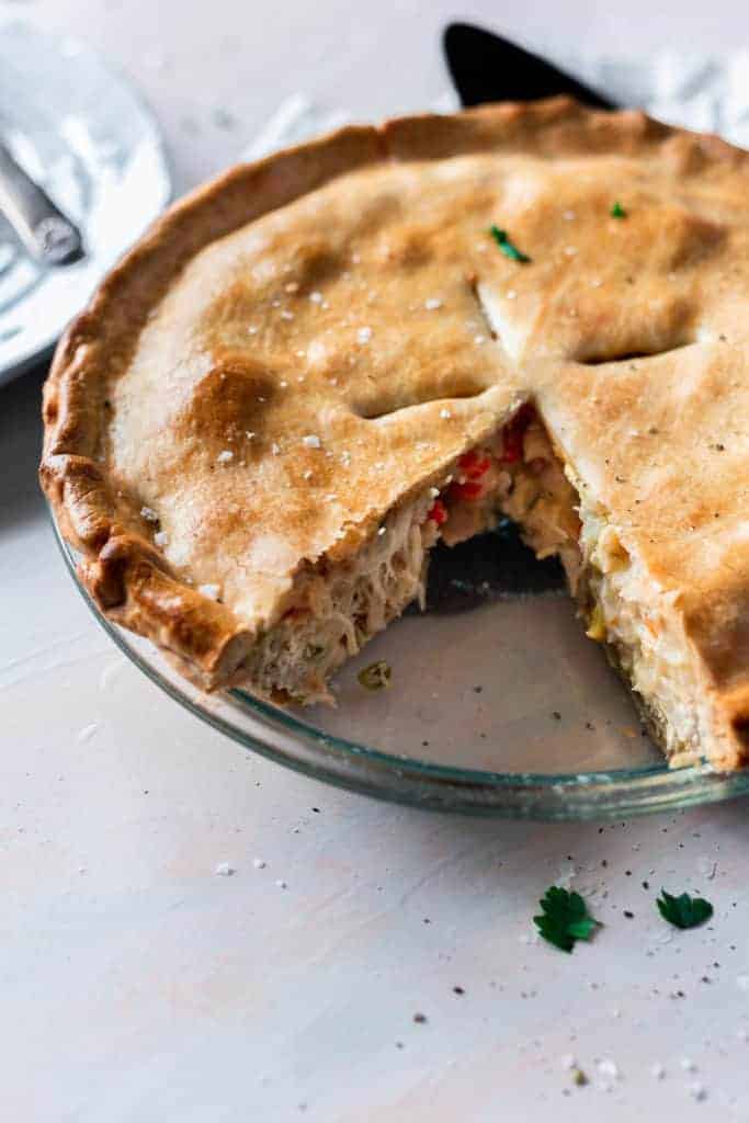 chicken pot pie in a clear pie pan with a golden crust and once slice taken out