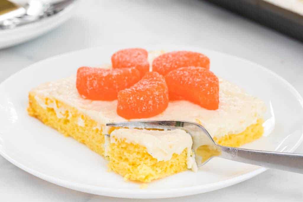thin orange cake slice with white icing and orange candies on top being cut with a fork