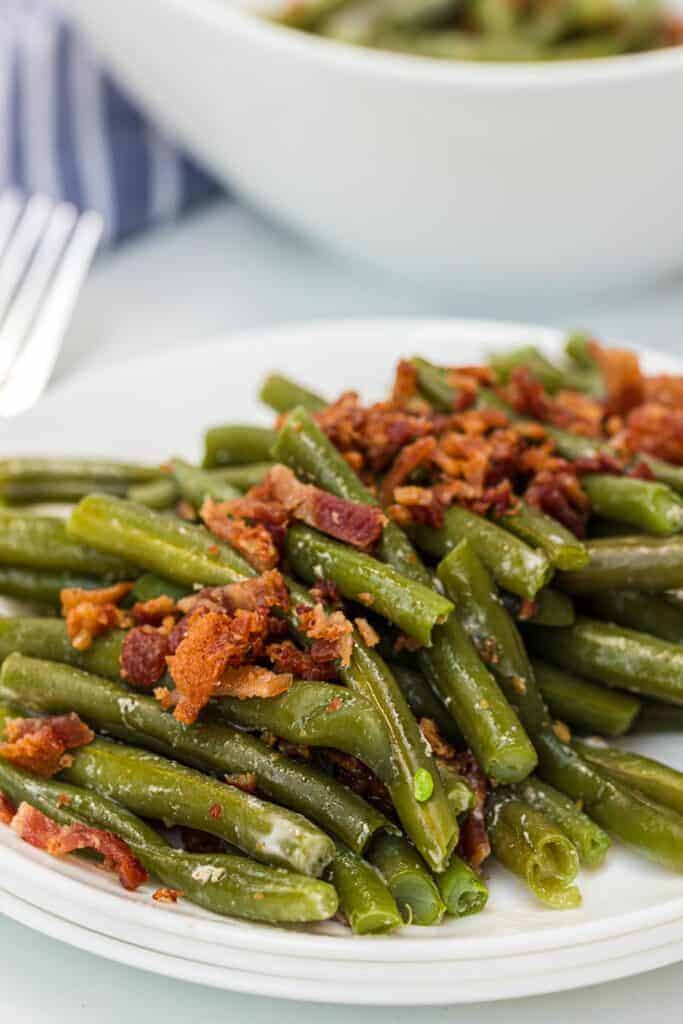 green beans on a white plate with bacon on top