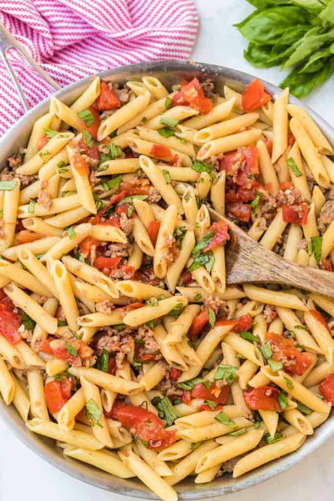 pene pasta with shredded cheese with tomatoes and herbs in a pan with a wooden spoon