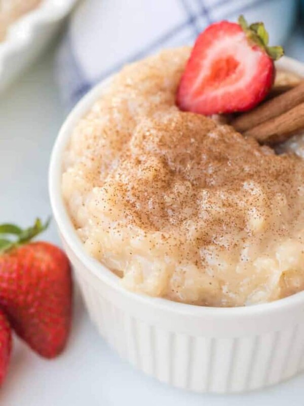 Rice pudding in white ramekin with strawberries and cinnamon sticks