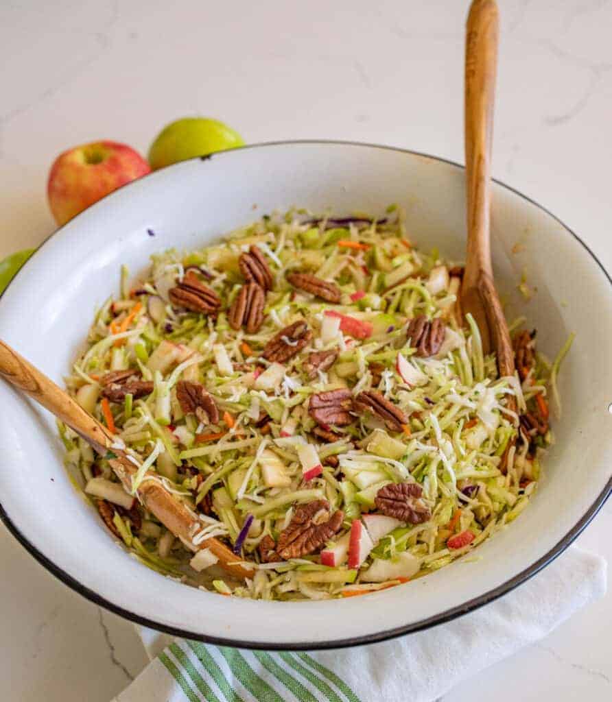 cabbage and apple salad with walnuts in a white bowl with two wooden spoons.