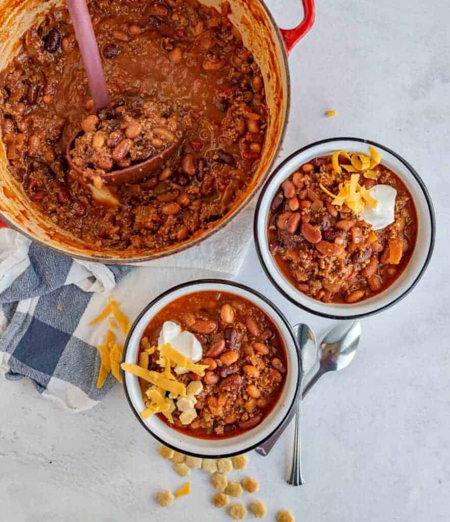 two bowls of chili in white bowls next to the dutch oven
