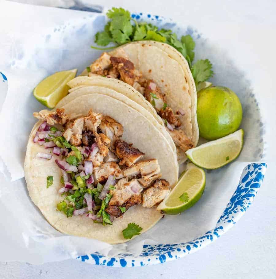 chicken tacos in two tortillas in bowl with cilantro and lime wedges