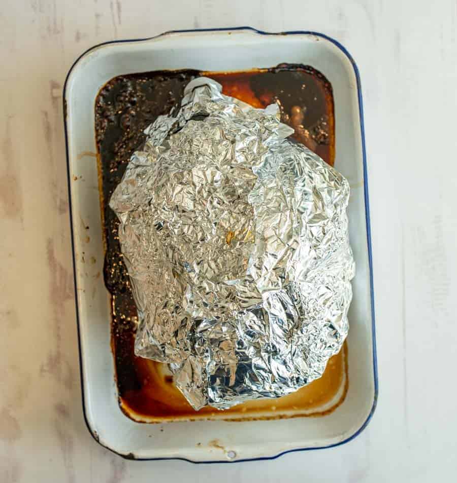 top view of whole ham wrapped in tin foil in a white dish