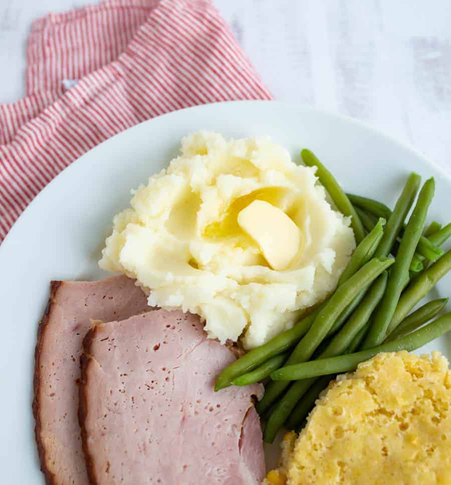 ham, green beans, stuffing and mashed potatoes on a white circular plate.