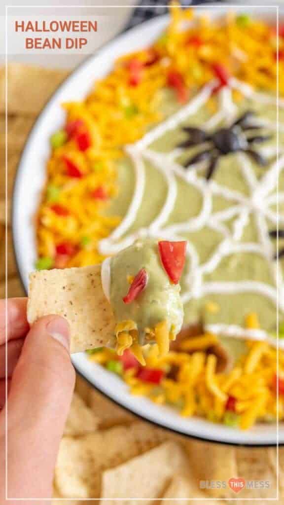 Text reads "halloween bean dip" over a sour cream spiderweb decorated dip bowl