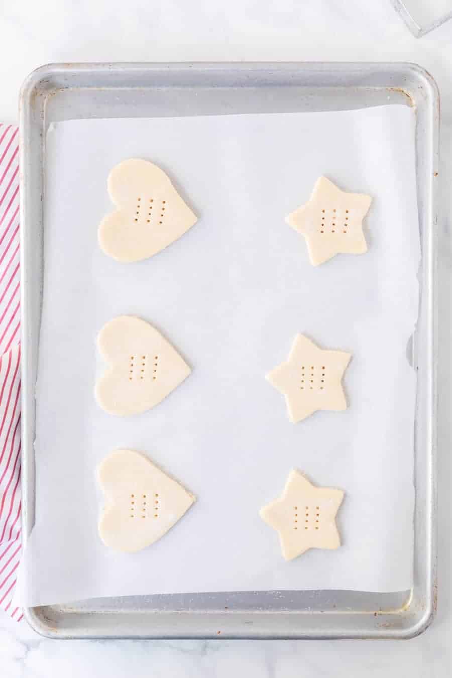 heart and start shaped shortbread cookies with fork punctures on a sheet pan top view not yet baked (top view).