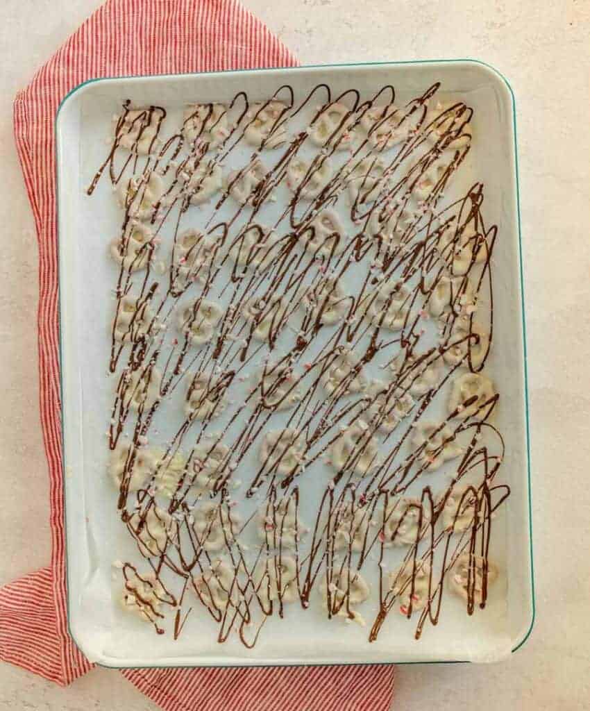 sheet pan of pretzels with white chocolate drizzled with milk chocolate and sprinkled with broken candy canes