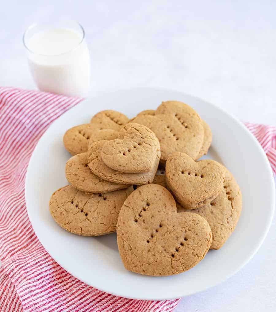 graham crackers in the shape of little hearts with fork punctures in them on a stack on a plate.