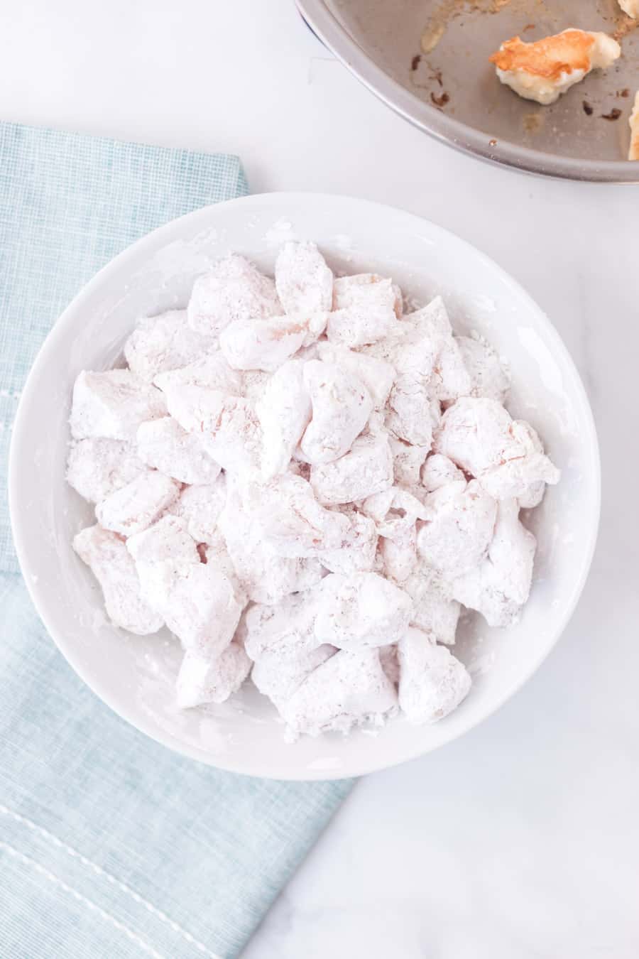 chicken pieces dusted in flour in a white bowl.