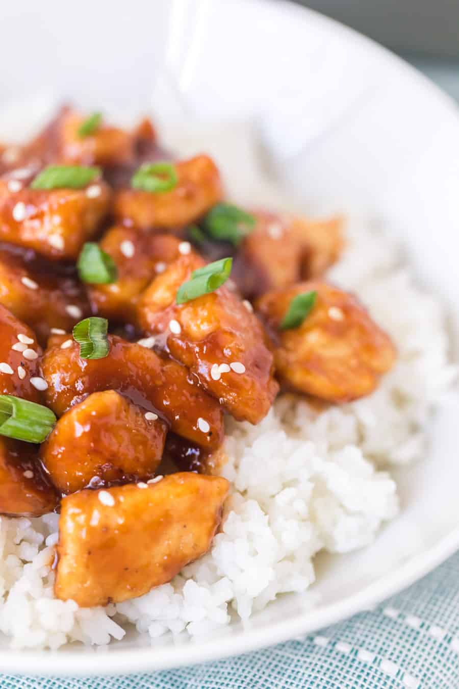 sticky general tso's chicken pieces over rice in a white bowl up close.