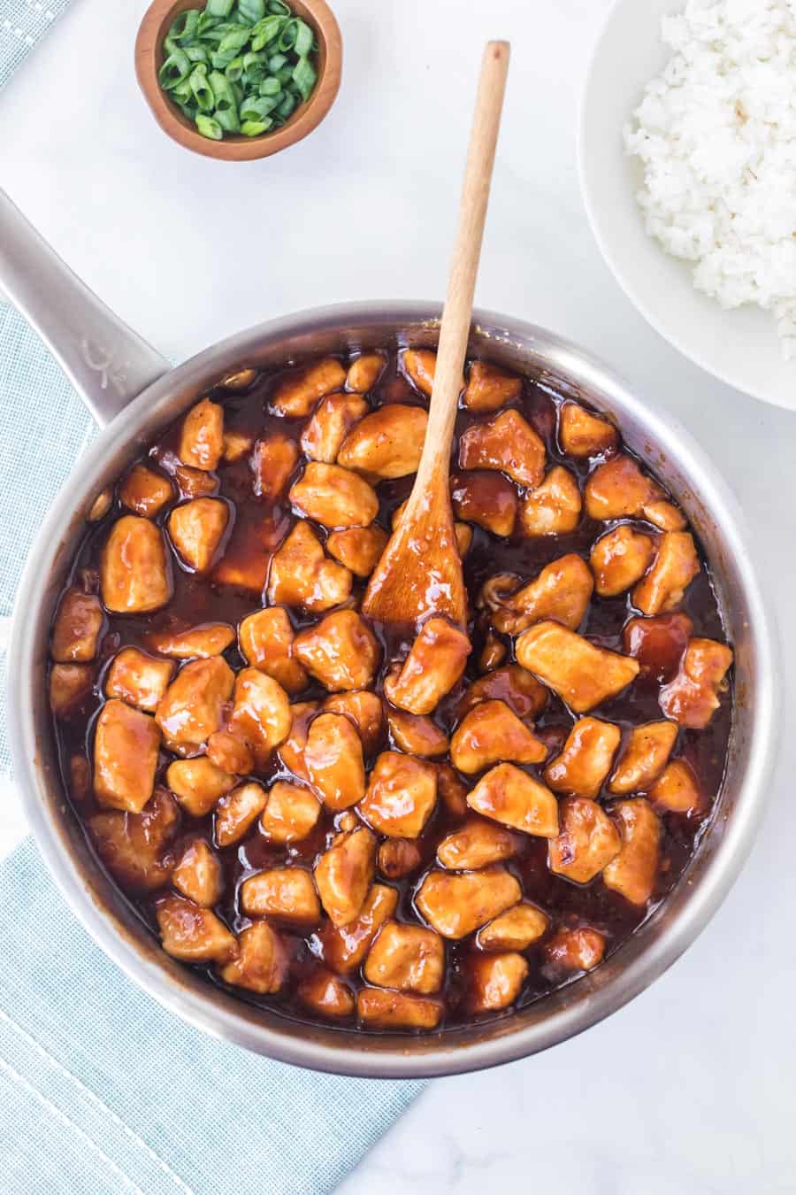 pan of sticky saucy general tso chicken pieces top view with a wooden spoon.