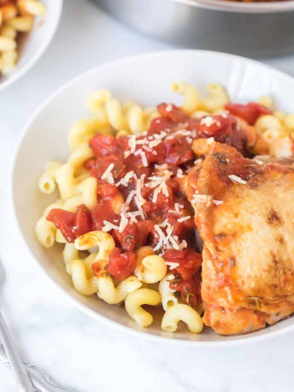 chicken with tomato sauce over garlic twisty pasta in a white bowl