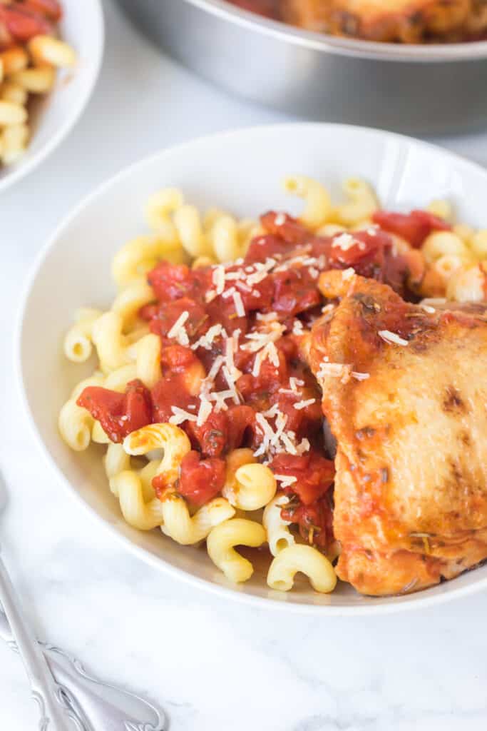 chicken with tomato sauce over garlic twisty pasta in a white bowl