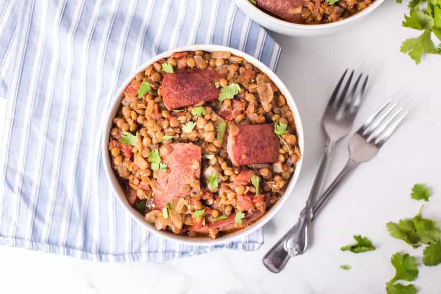 top view of 2 white bowls of spicy lentils and sausage with a spoon