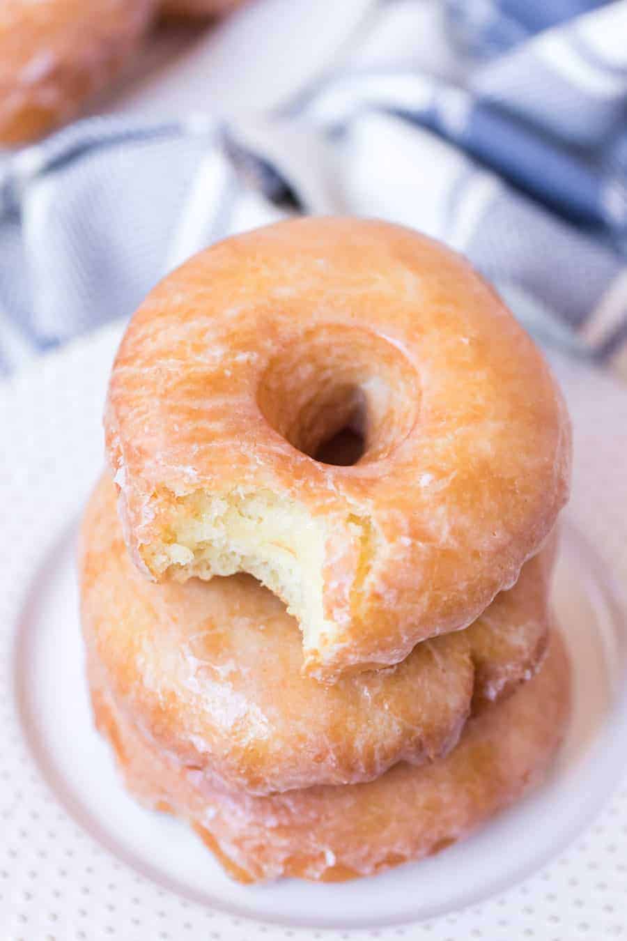 Top view of a stack of three old fashioned glazed doughnuts with the top one having a bite taken out.