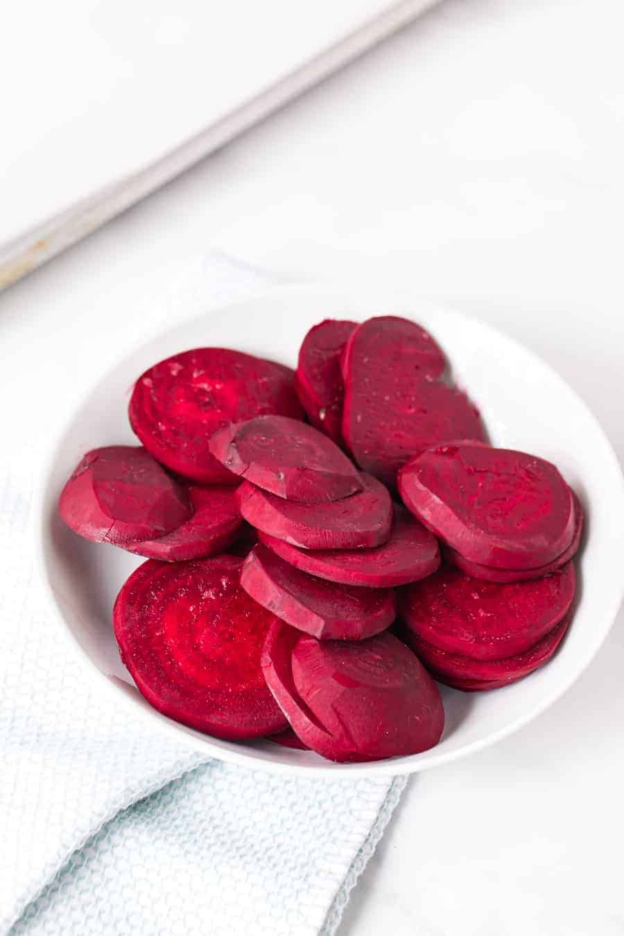 a bowl of piled up raw red beets sliced into thin rounds.