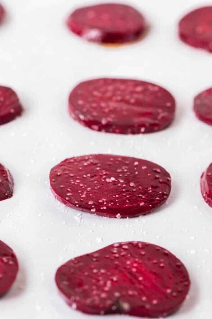 close up view of a baking sheet with slices of round and thin raw beets ready to be baked