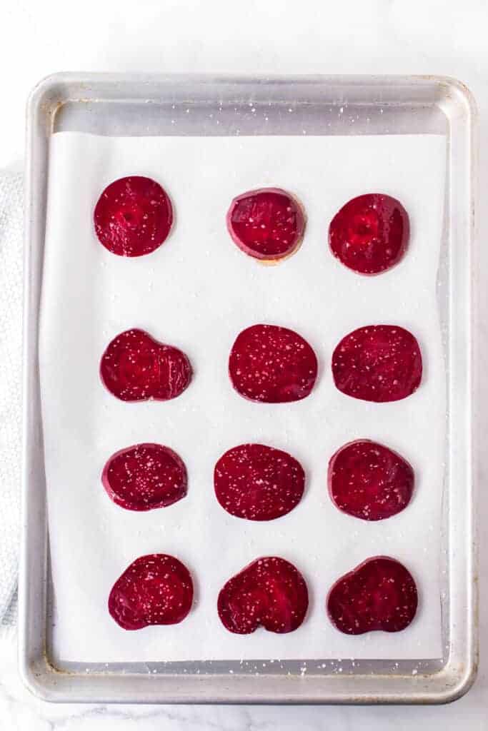 top view of a baking sheet with slices of round and thin raw beets ready to be baked